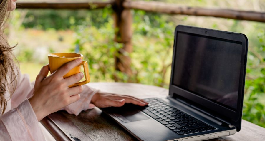 Person working on a laptop with coffee in a relaxed outdoor setting, illustrating remote work